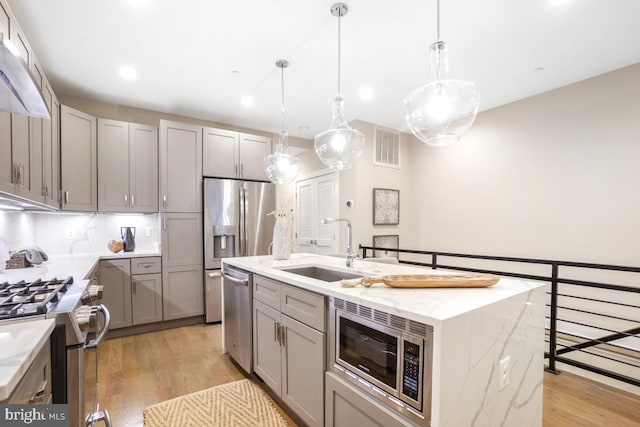 kitchen featuring pendant lighting, sink, appliances with stainless steel finishes, a kitchen island with sink, and light stone countertops