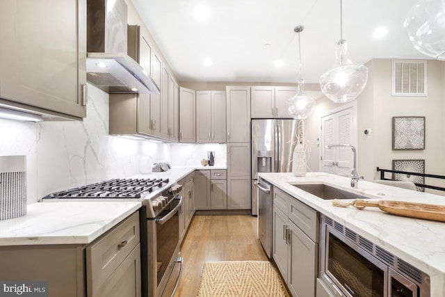 kitchen featuring sink, gray cabinetry, decorative light fixtures, appliances with stainless steel finishes, and wall chimney range hood