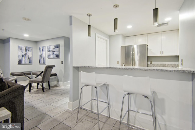 kitchen featuring hanging light fixtures, light stone countertops, stainless steel refrigerator, white cabinetry, and kitchen peninsula