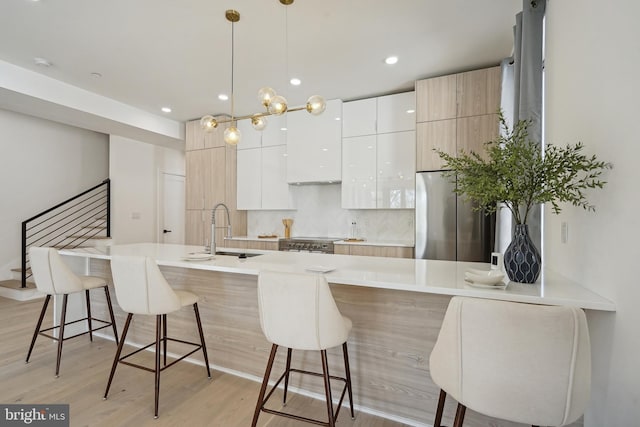 kitchen with a kitchen bar, sink, appliances with stainless steel finishes, pendant lighting, and white cabinets