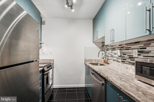 kitchen with sink, appliances with stainless steel finishes, tasteful backsplash, blue cabinets, and dark tile patterned flooring