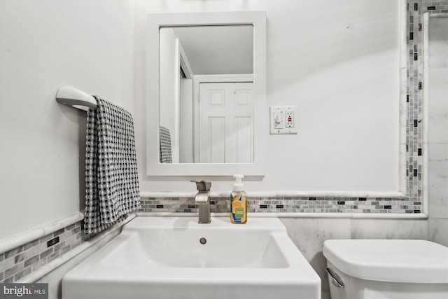 bathroom with toilet, sink, and tile walls