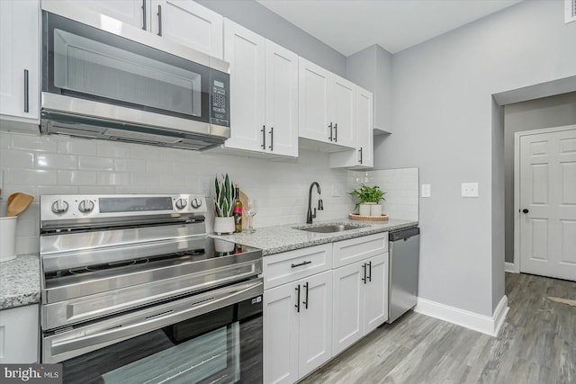 kitchen featuring sink, white cabinetry, appliances with stainless steel finishes, light stone countertops, and backsplash