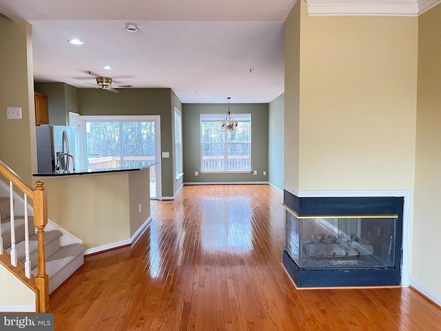 unfurnished living room with ceiling fan with notable chandelier, light hardwood / wood-style flooring, and a multi sided fireplace