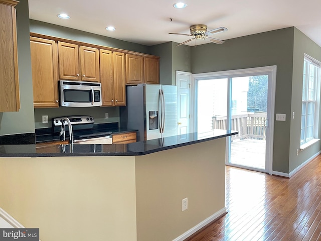 kitchen with appliances with stainless steel finishes, kitchen peninsula, dark stone counters, ceiling fan, and light hardwood / wood-style floors