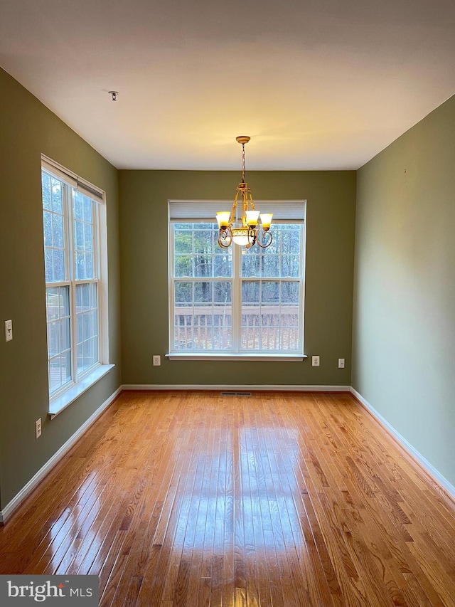 unfurnished dining area featuring a wealth of natural light, an inviting chandelier, and light wood-type flooring