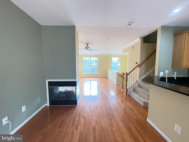 unfurnished living room featuring sink, crown molding, ceiling fan, hardwood / wood-style floors, and a multi sided fireplace