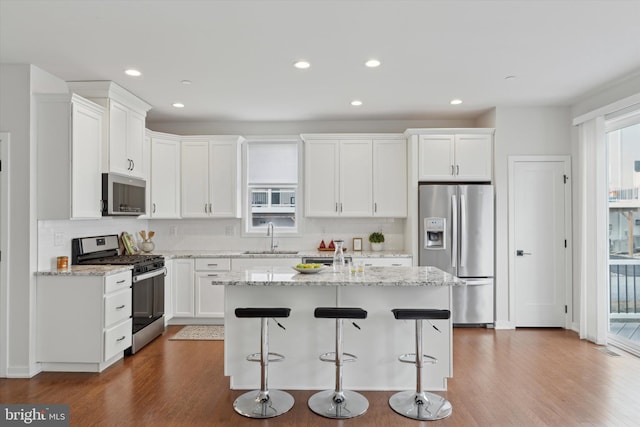 kitchen with stainless steel appliances, light stone countertops, a kitchen island, and white cabinetry