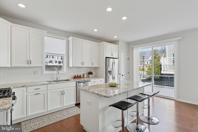 kitchen featuring sink, white cabinetry, a center island, appliances with stainless steel finishes, and light stone countertops