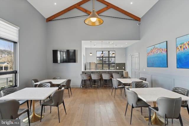 dining space with beamed ceiling, high vaulted ceiling, and light wood-type flooring