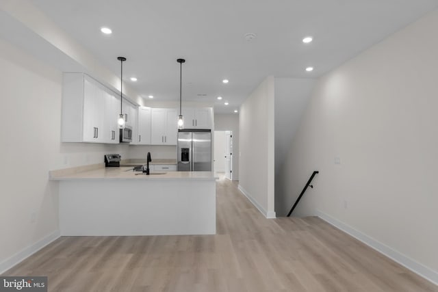 kitchen with appliances with stainless steel finishes, pendant lighting, white cabinets, kitchen peninsula, and light wood-type flooring