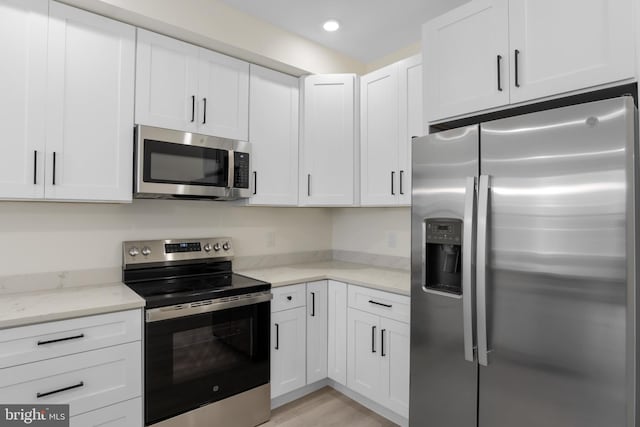 kitchen with light stone counters, stainless steel appliances, light wood-type flooring, and white cabinets