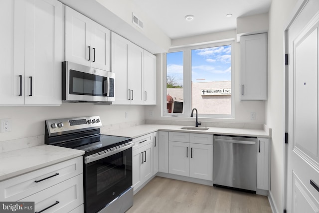 kitchen with appliances with stainless steel finishes, white cabinetry, sink, light stone countertops, and light hardwood / wood-style flooring