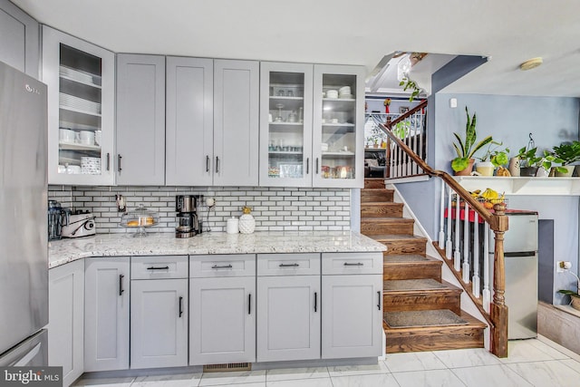 kitchen with light stone counters, decorative backsplash, gray cabinets, and stainless steel refrigerator