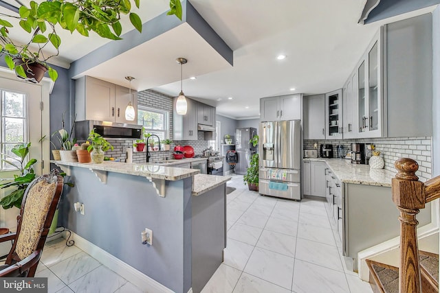 kitchen with appliances with stainless steel finishes, gray cabinetry, hanging light fixtures, a kitchen bar, and kitchen peninsula