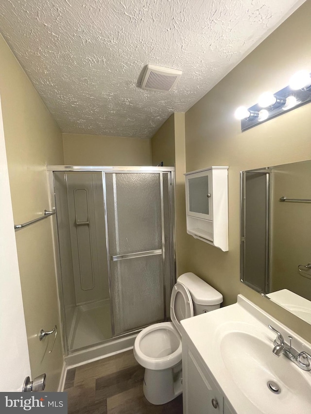 full bath with a textured ceiling, toilet, wood finished floors, visible vents, and a shower stall