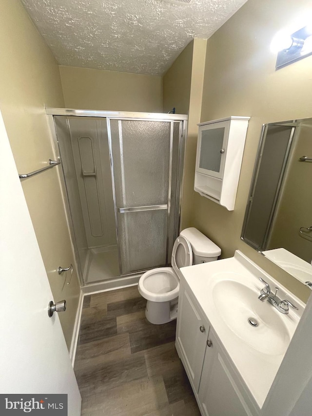 full bathroom with toilet, wood finished floors, a textured ceiling, vanity, and a shower stall