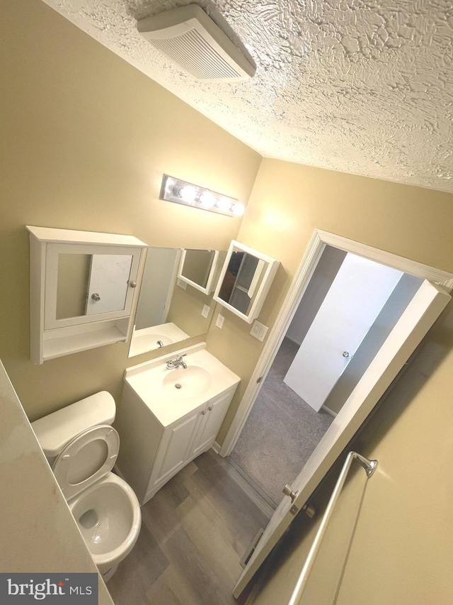 bathroom featuring visible vents, toilet, wood finished floors, a textured ceiling, and vanity