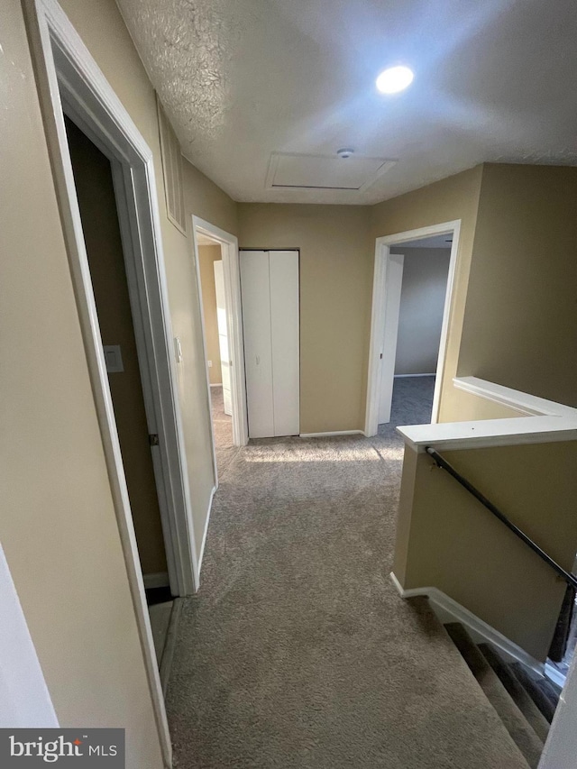 hallway featuring carpet floors, attic access, an upstairs landing, and baseboards