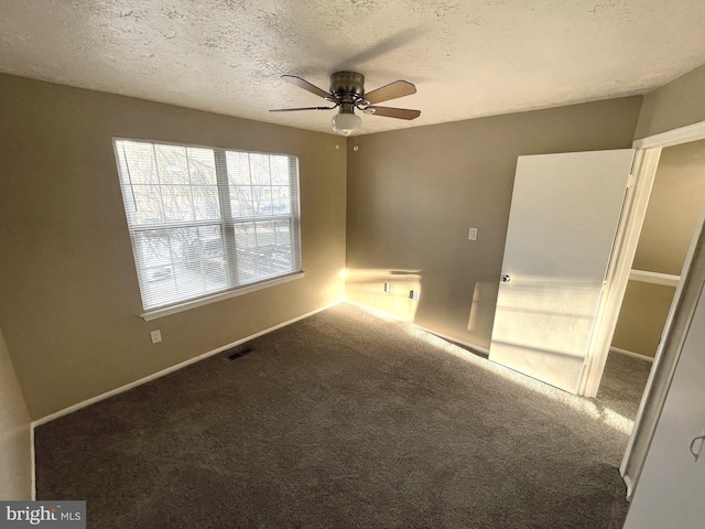 carpeted empty room with baseboards, ceiling fan, visible vents, and a textured ceiling