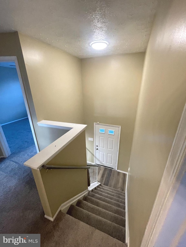 stairs featuring a textured ceiling and carpet flooring