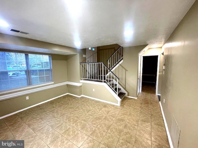 unfurnished room with baseboards, stairs, visible vents, and a textured ceiling