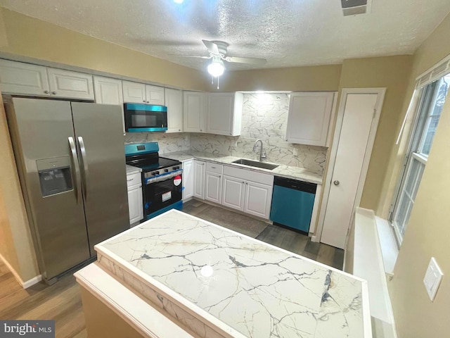 kitchen with dark wood-style floors, backsplash, appliances with stainless steel finishes, white cabinetry, and a sink