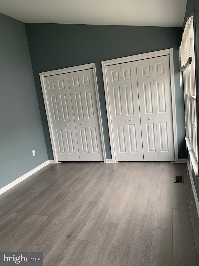 unfurnished bedroom with hardwood / wood-style floors, lofted ceiling, and two closets