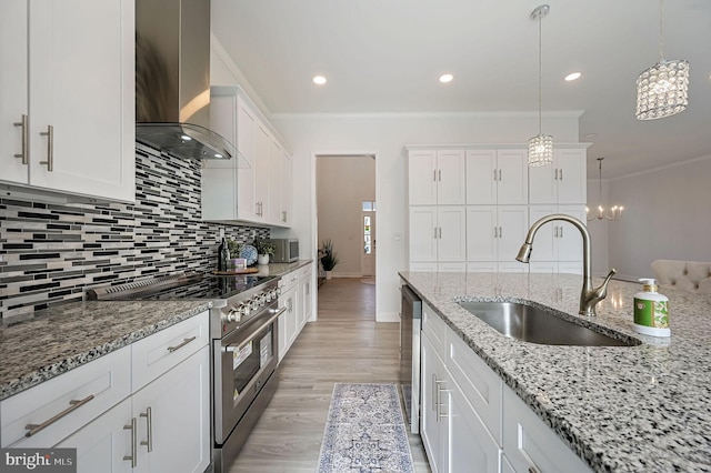 kitchen featuring sink, appliances with stainless steel finishes, pendant lighting, wall chimney range hood, and white cabinets