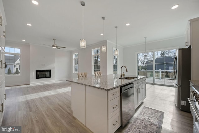 kitchen with sink, light stone counters, hanging light fixtures, appliances with stainless steel finishes, and an island with sink