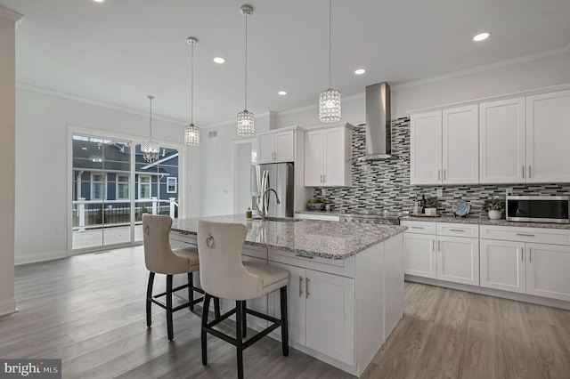 kitchen featuring white cabinetry, wall chimney exhaust hood, and a center island with sink