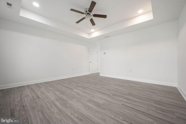 empty room featuring ceiling fan, wood-type flooring, and a tray ceiling