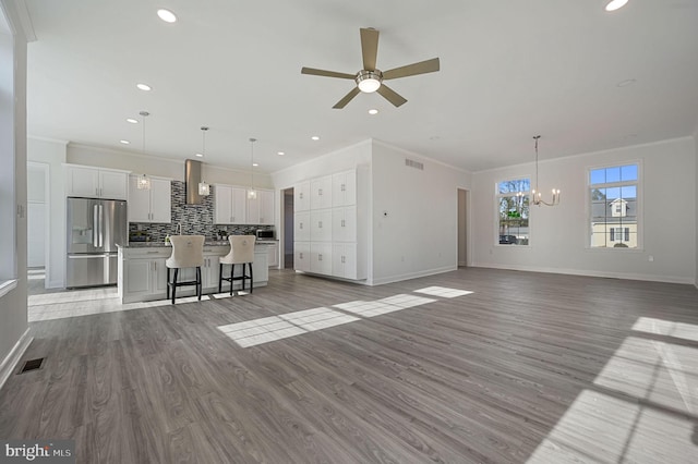 unfurnished living room with ornamental molding, ceiling fan with notable chandelier, and light wood-type flooring