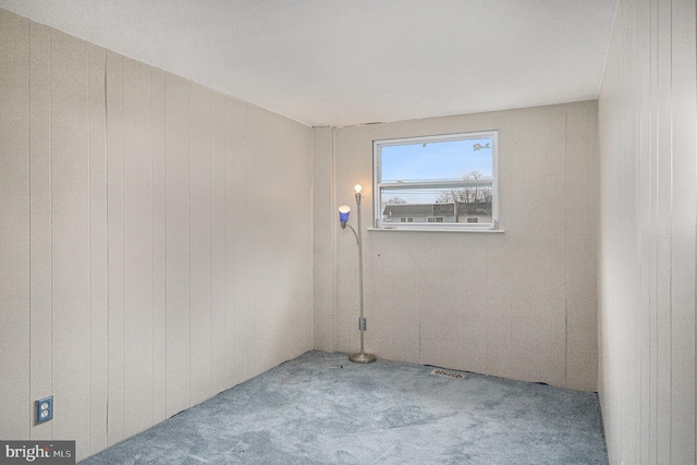 empty room featuring light carpet and wood walls