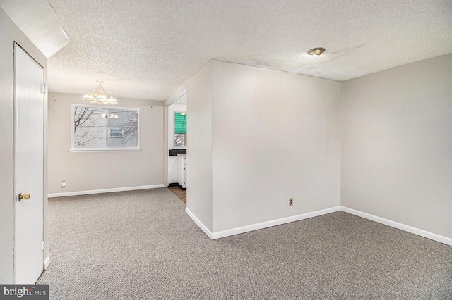 carpeted empty room featuring a textured ceiling and a chandelier