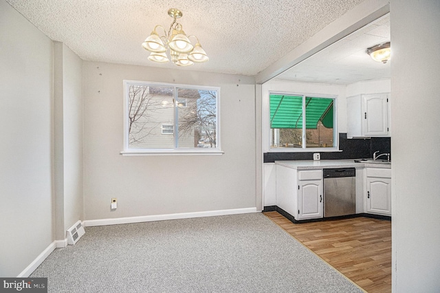 kitchen with white cabinetry, sink, hanging light fixtures, stainless steel dishwasher, and a textured ceiling