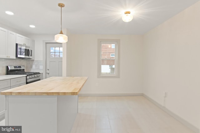 kitchen with appliances with stainless steel finishes, pendant lighting, wood counters, white cabinetry, and backsplash