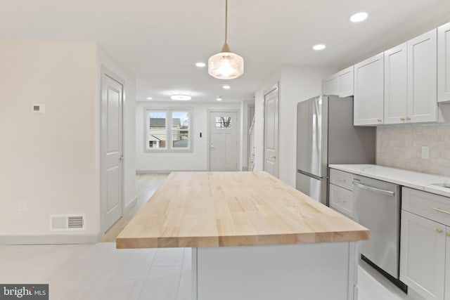 kitchen with wooden counters, decorative light fixtures, a center island, appliances with stainless steel finishes, and backsplash