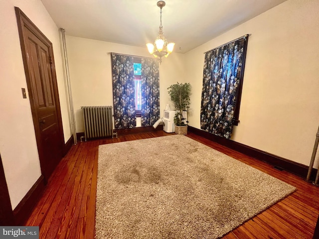 unfurnished room featuring radiator, a notable chandelier, and dark hardwood / wood-style flooring