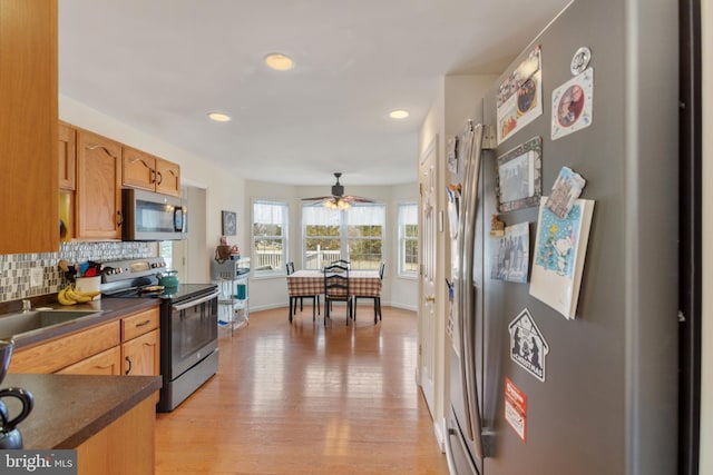 kitchen with appliances with stainless steel finishes, sink, backsplash, ceiling fan, and light wood-type flooring