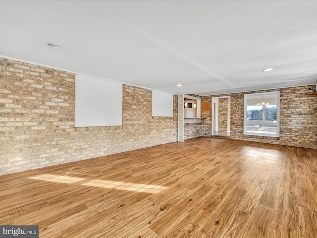 unfurnished living room with brick wall and light wood-type flooring