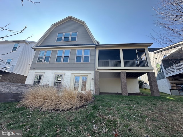 rear view of property with a sunroom, a yard, brick siding, and a gambrel roof