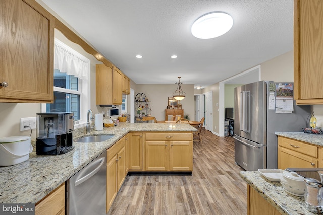 kitchen with sink, appliances with stainless steel finishes, kitchen peninsula, pendant lighting, and light hardwood / wood-style floors