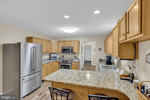 kitchen featuring sink, a breakfast bar area, appliances with stainless steel finishes, light stone countertops, and kitchen peninsula