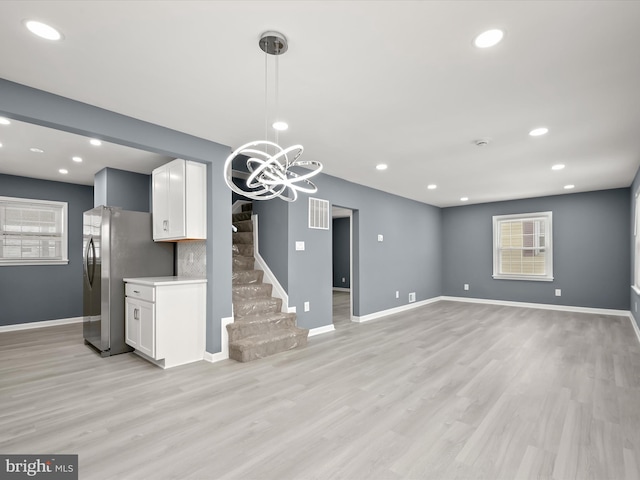 unfurnished living room with an inviting chandelier and light wood-type flooring