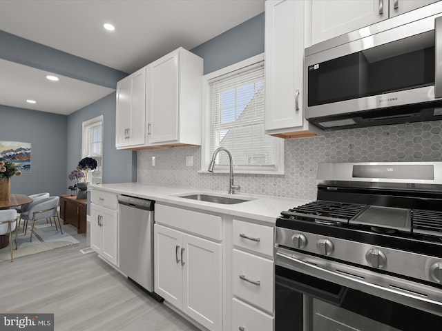 kitchen featuring sink, white cabinetry, tasteful backsplash, light wood-type flooring, and appliances with stainless steel finishes