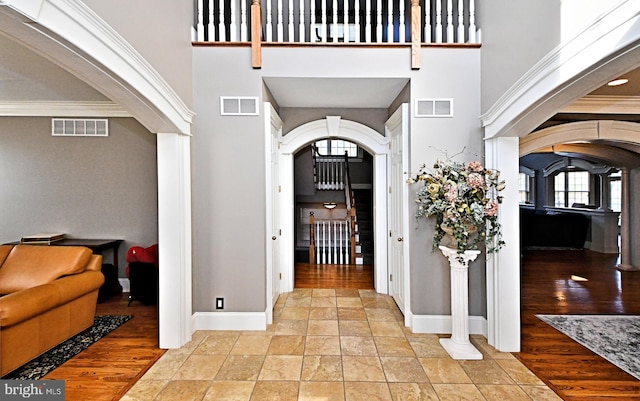 entrance foyer featuring a towering ceiling, ornamental molding, and light wood-type flooring