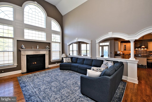 living room featuring dark hardwood / wood-style flooring, high vaulted ceiling, and decorative columns