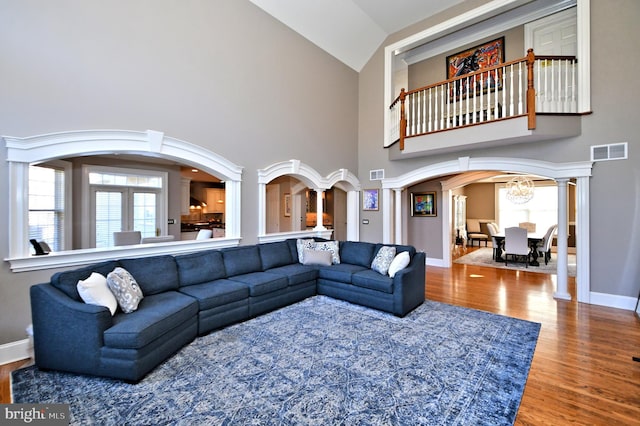 living room with high vaulted ceiling, a wealth of natural light, decorative columns, and wood-type flooring