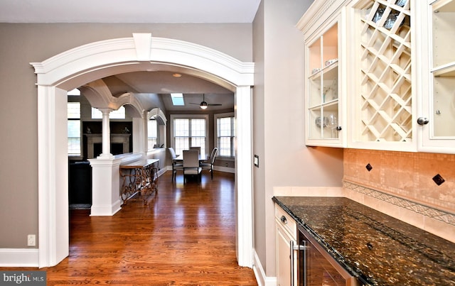 interior space with decorative columns, wine cooler, dark hardwood / wood-style flooring, decorative backsplash, and dark stone counters